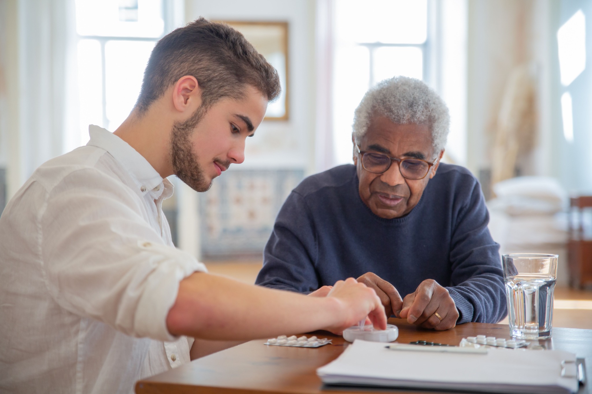 An older Black man and a younger white man reviewing medication together at home