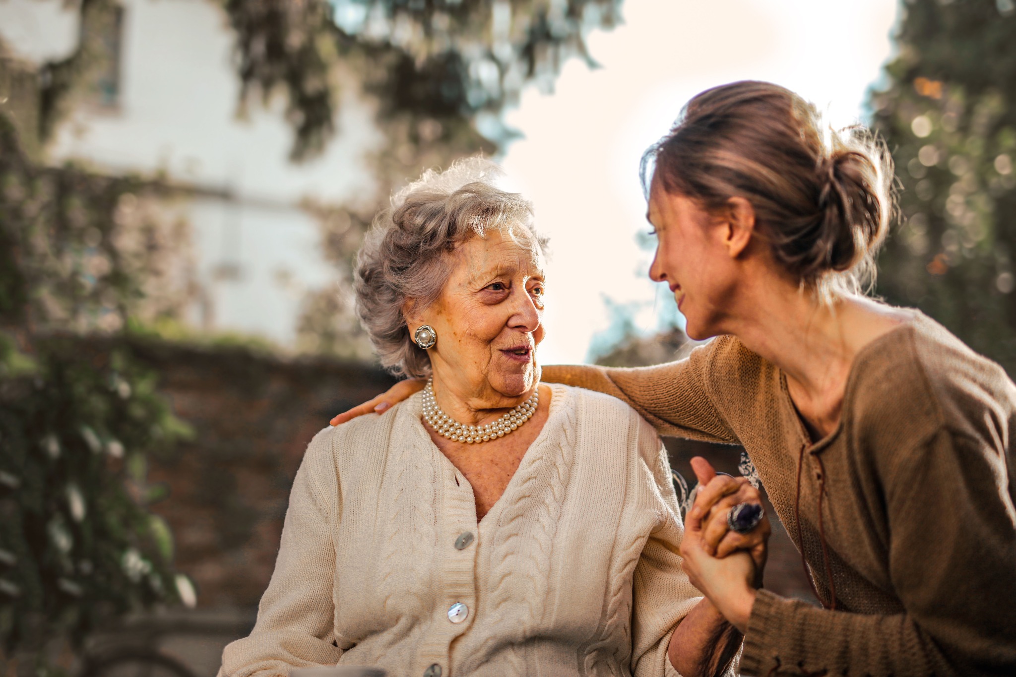 An older woman and a younger woman sharing a warm conversation outdoors